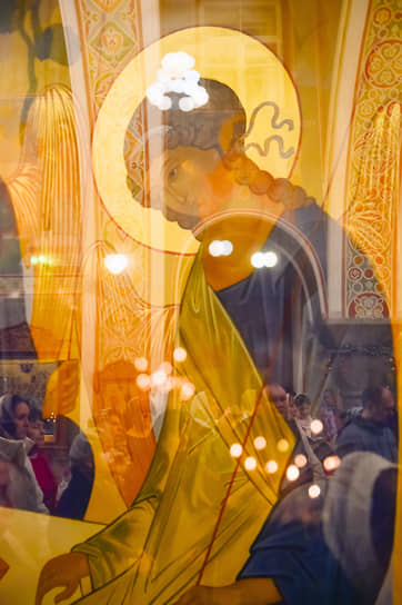 Верующие в отражении иконы «Троица» Андрея Рублева на пасхальном богослужении в храме Святого Иоанна Предтечи в Красноярске