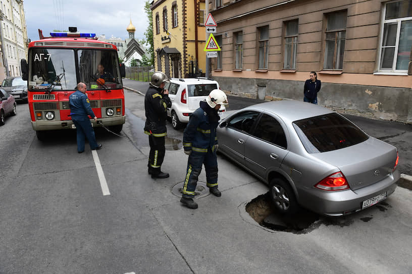 Сотрудники МЧС осматривают провал грунта под автомобилем в центре города