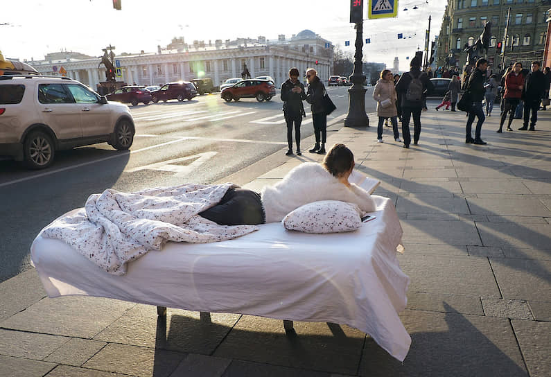 Девушка лежит в постели на Невском проспекте и читает книгу, призывая к добровольной самоизоляции из-за пандемии коронавируса COVID-19