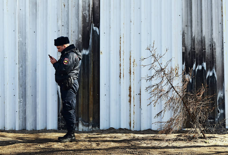 Полицейский с мобильным телефоном у забора, закрывающего несанкционированную свалку