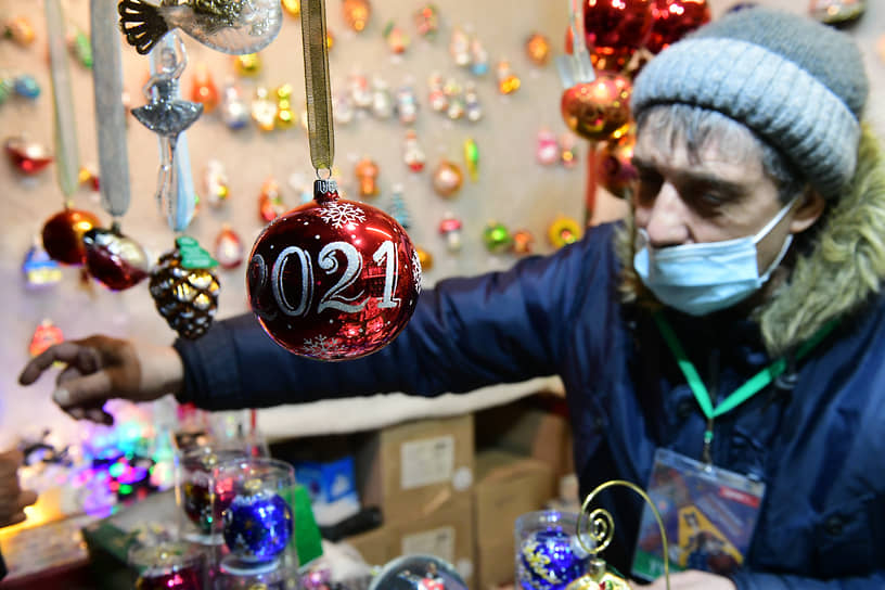 Елочный шар 2021 на фоне продавца новогодних украшений