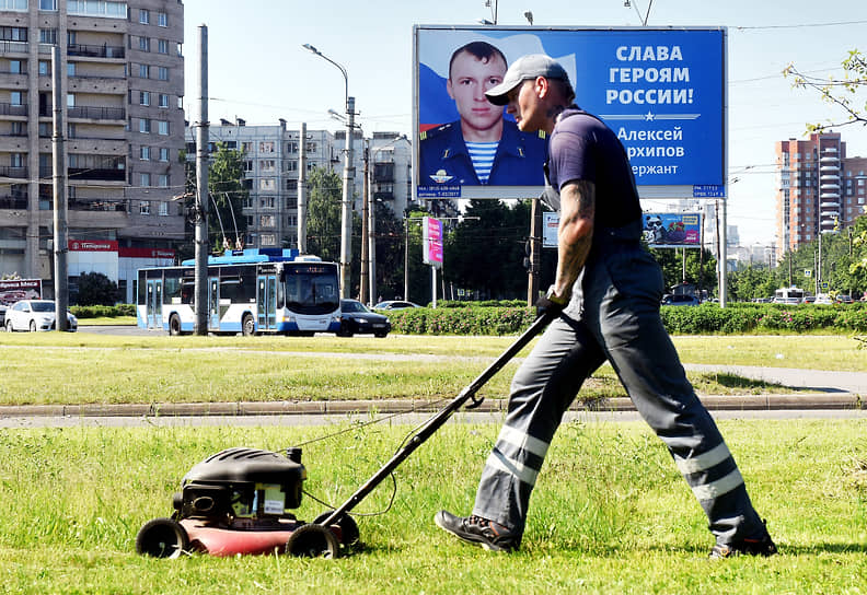 Газонокосильщик косит траву на фоне билборда с портретом военнослужащего уничтожившего во время специальной военной операции в Украине 11 единиц боевой техники