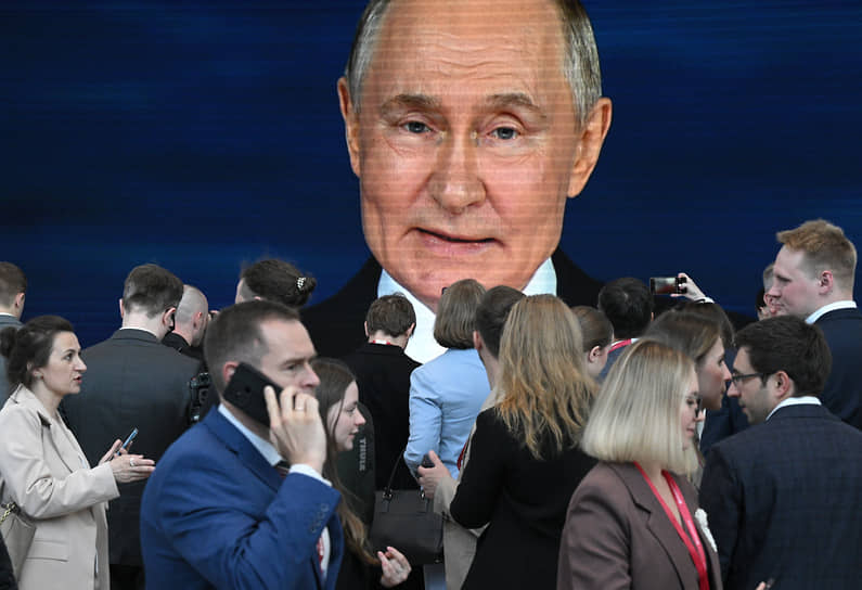 Участники форума смотрят по телевизору выступление президента России Владимира Путина на пленарном заседании 