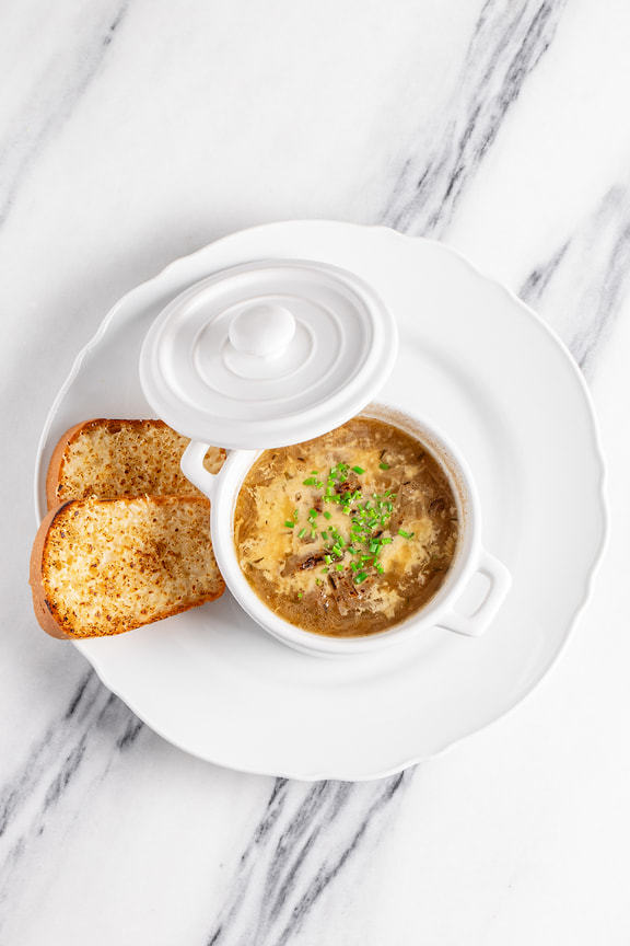 В французский луковый суп шеф-повар добавляет херес и сервирует блюдо с гренками бриошь
