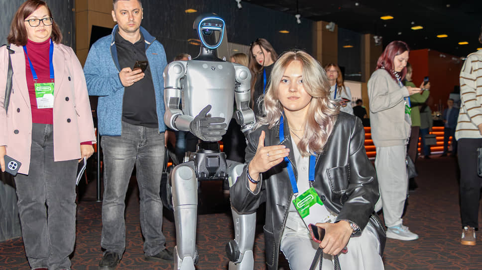 Посетительница фотографируется с роботом, демонстрирующим жест одобрения, на форуме «Цифроземье» в Воронеже