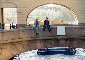 Зимняя канава, молодая пара сидит на мосту, свесив ноги над водой