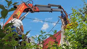Работа электрика в рабочей люльке на автоподъёмнике Palfinger во время монтажа провода линии электроснабжения домов дачного посёлка