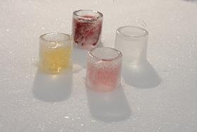 Рюмки изо льда с разноцветной жидкостью на снегу. Бутылка водки Nemiroff в снегу